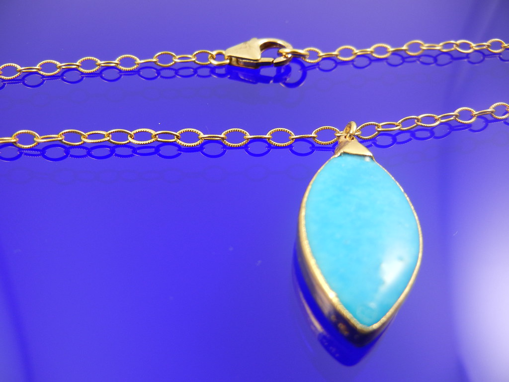 Gold and turquoise pendant necklace worn long, symbol of transformation and femininity